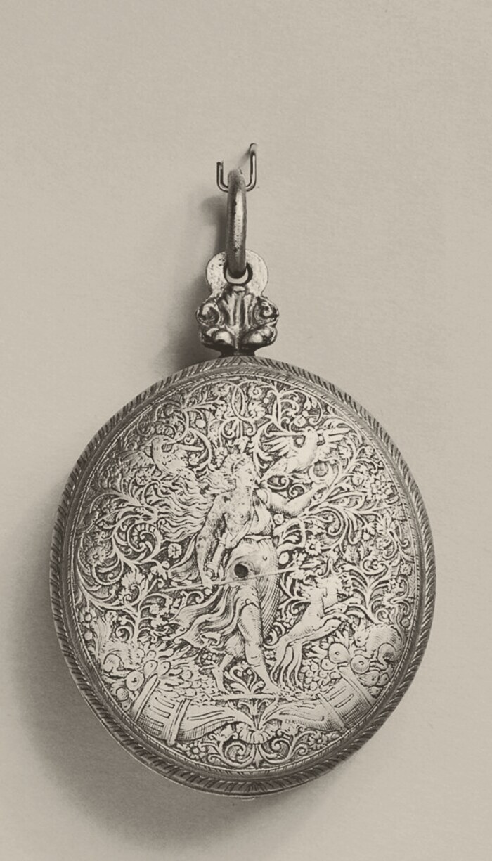 An oval watch case hanging from a ring and pendant, its whole surface engraved with scrolling foliage around a standing female figure with a peacock beside her.